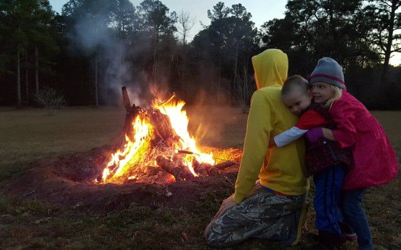 two kids hugging their dad outside at night by a fire