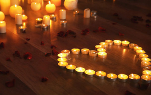 Сердце из зажженных свечей на полу. Рядом лепестки роз и другие свечи